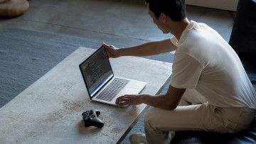 A man opening the Surface Studio Laptop with an Xbox Wireless Controller next to it